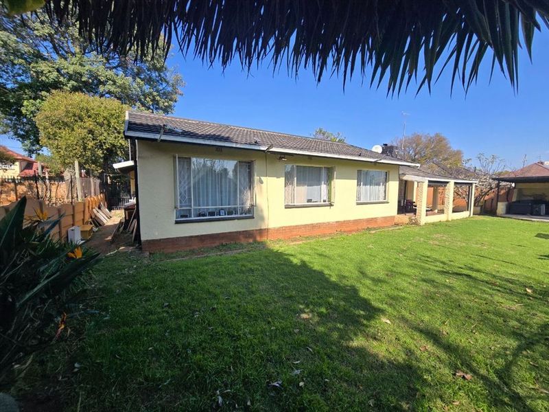 Rear view of the house featuring a tiled roof, plastered exterior walls, and a covered patio area overlooking the garden.
