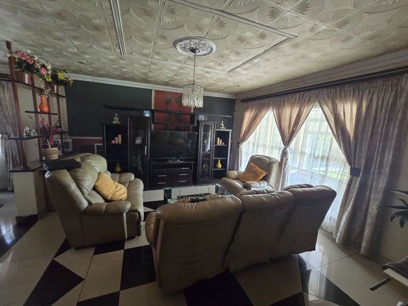 A living room featuring patterned ceiling tiles, a central ceiling rose, and tiled flooring, providing a dated but functional living space.