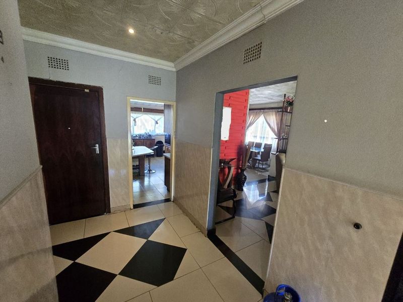 A central hallway featuring geometric tiled flooring, wall tiling, and access to adjacent living and kitchen areas.