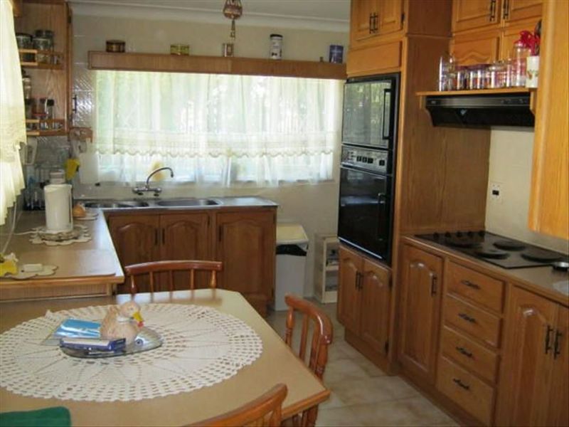 A functional kitchen featuring timber cabinetry, built-in appliances including an oven and microwave, and a double bowl sink with a large window.