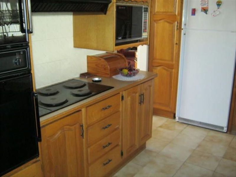 A dated kitchen featuring traditional wooden cabinetry, built-in oven, electric hob, and tiled flooring, offering potential for a modern renovation.