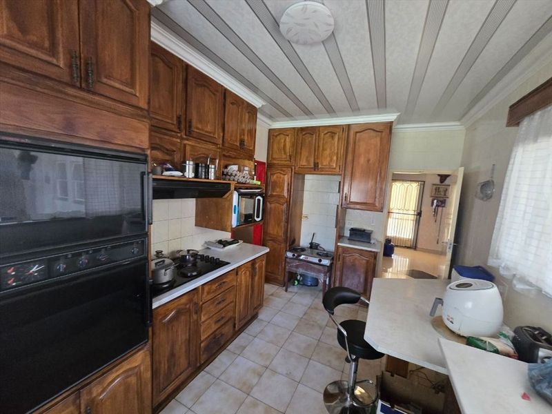 A functional kitchen featuring traditional wooden cabinetry, built-in oven, hob, and tiled flooring, offering a classic layout with potential for modern updates.