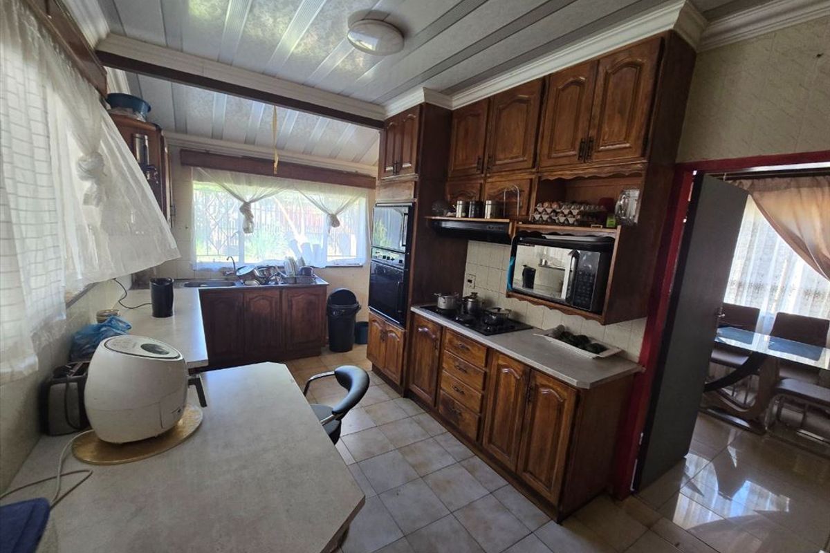 A functional kitchen featuring traditional wooden cabinetry, built-in appliances, tiled flooring, and ample counter space, offering potential for a modern renovation.