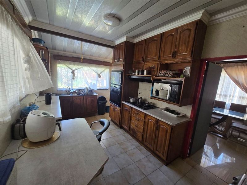 A functional kitchen featuring traditional wooden cabinetry, built-in appliances, tiled flooring, and ample counter space, offering potential for a modern renovation.