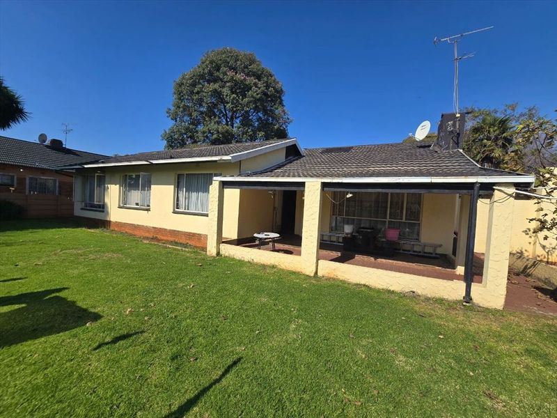 Rear view of the house featuring a covered patio area, tiled roof, and a spacious garden lawn.