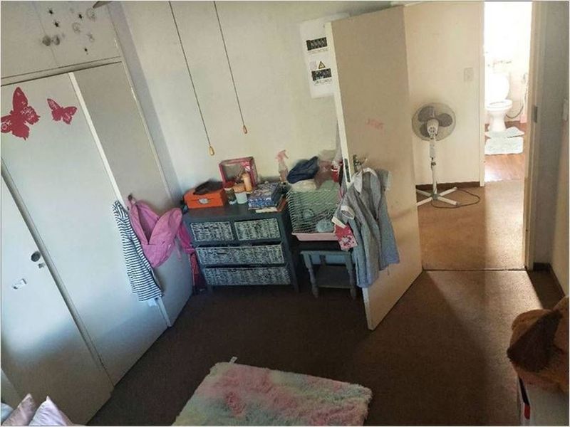 A bedroom featuring a built-in wardrobe, showing signs of wear on the walls and flooring, with an adjacent view into a bathroom.
