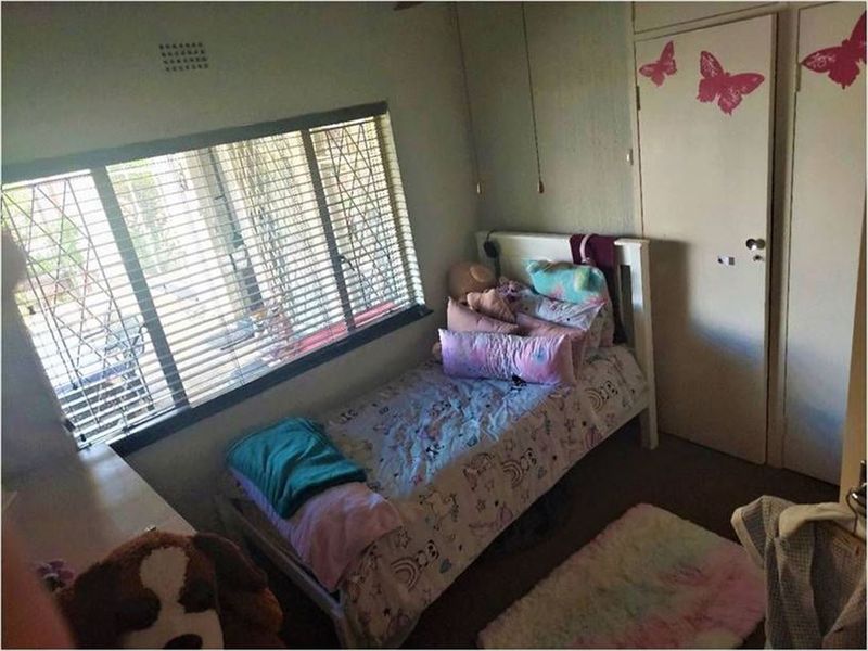 A standard bedroom featuring built-in cupboards, security bars on the window, and venetian blinds.