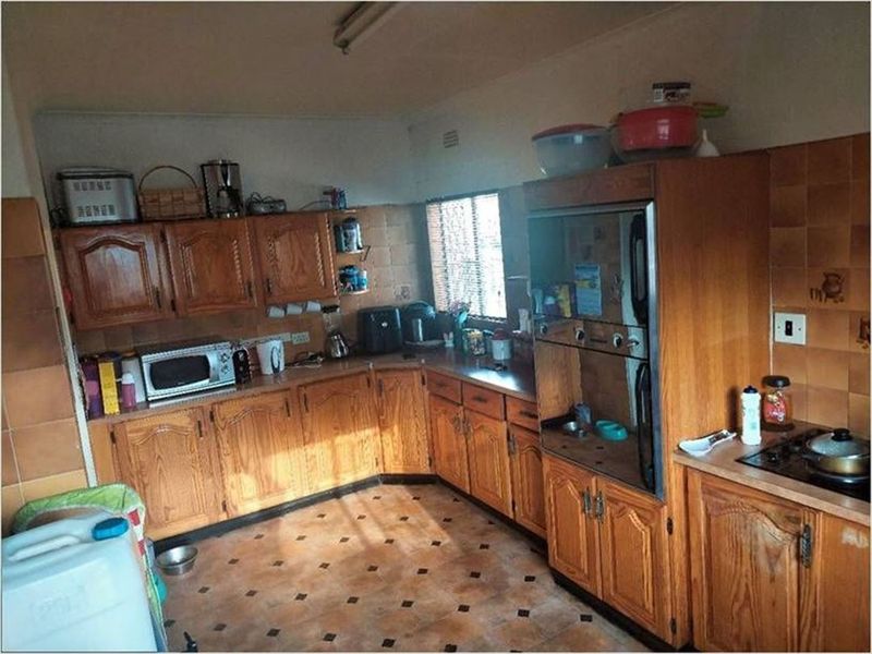 A dated kitchen featuring wooden cabinetry, built-in oven, hob, and tiled finishes, offering significant potential for a modern renovation.
