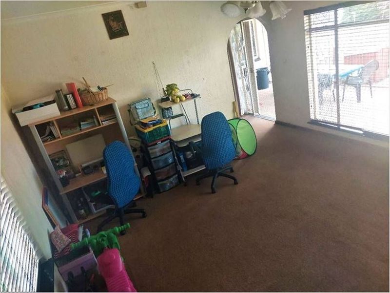 A living room area featuring an arched doorway, carpet flooring, and venetian blinds, currently used as a multi-purpose space.