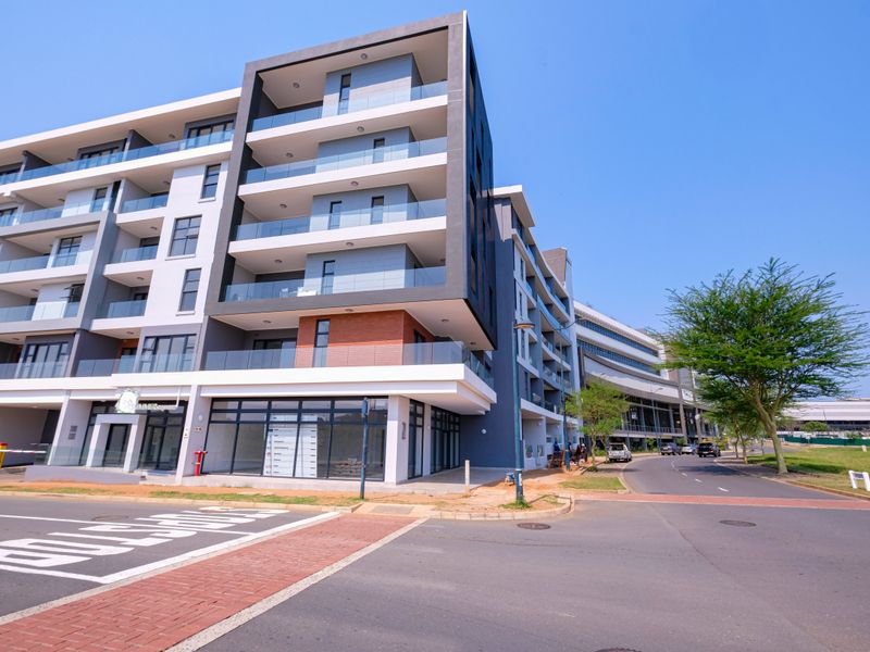 Modern multi-story apartment building featuring contemporary architectural design, glass balconies, and ground-floor commercial space situated on a corner lot.