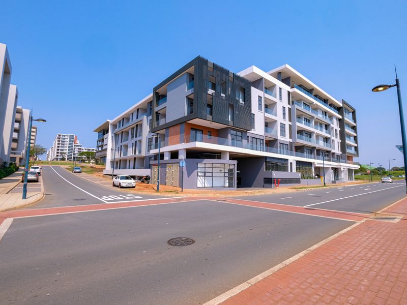 A modern multi-story apartment complex viewed from the street corner, showcasing contemporary architectural design and glass balcony features.