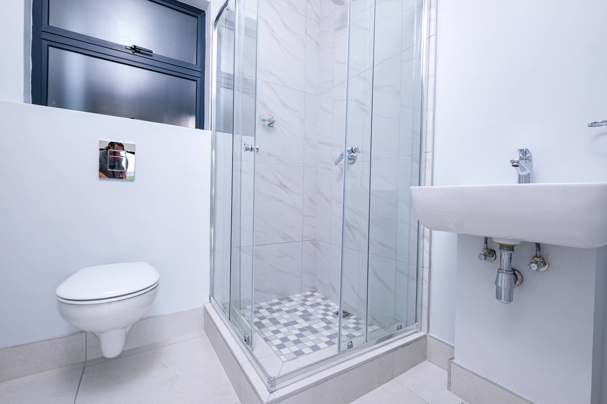 Modern bathroom featuring a wall-mounted toilet, a glass-enclosed shower with tiled finishes, and a wall-mounted basin with chrome fixtures.
