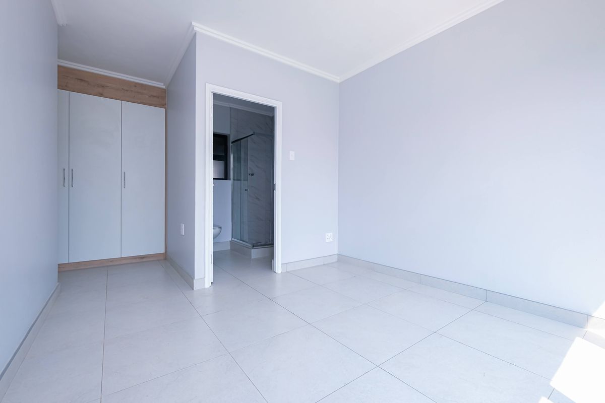 A bright, empty bedroom featuring neutral tiled flooring, built-in cupboards, and direct access to an en-suite bathroom.