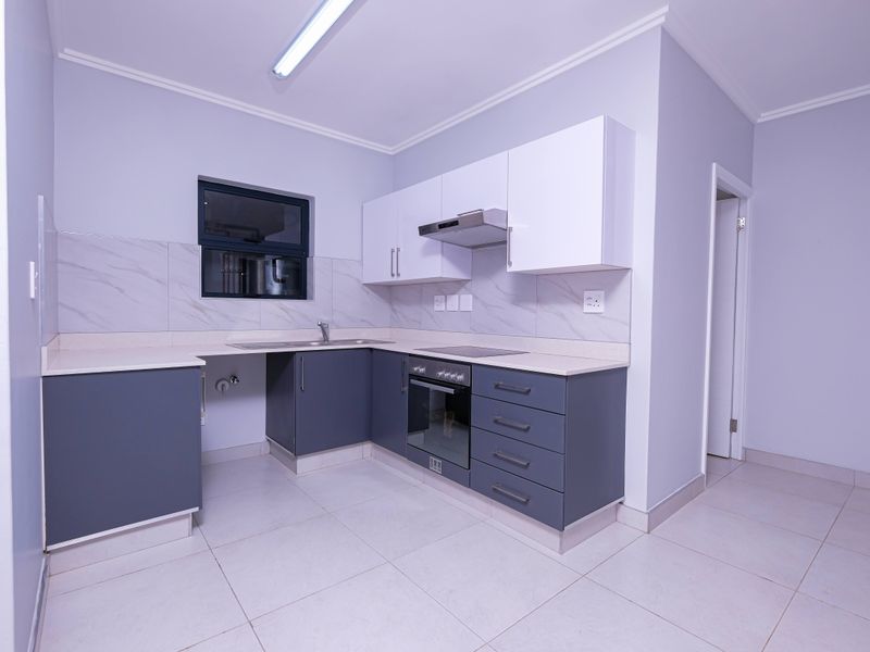 A clean, modern kitchen featuring grey lower cabinets, white upper cabinets, stone countertops, and integrated appliances including an oven and extractor fan.