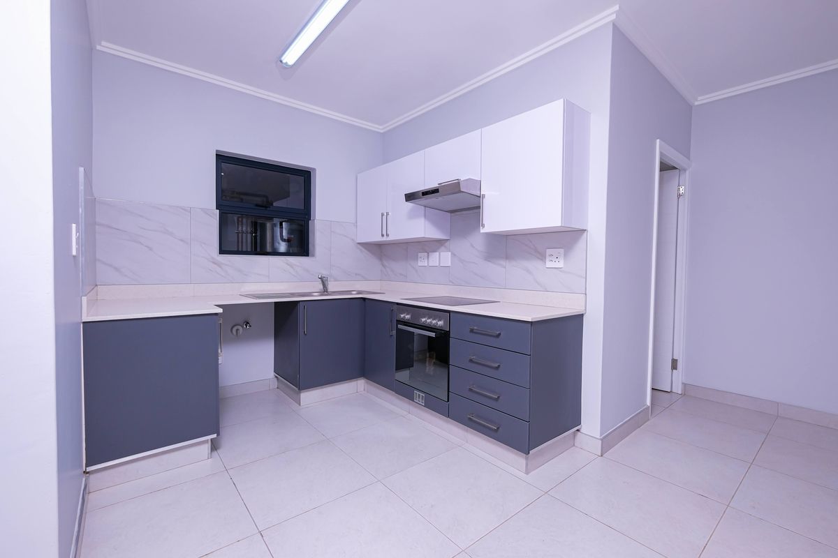 A clean, modern kitchen featuring grey lower cabinets, white upper cabinets, stone countertops, and integrated appliances including an oven and extractor fan.