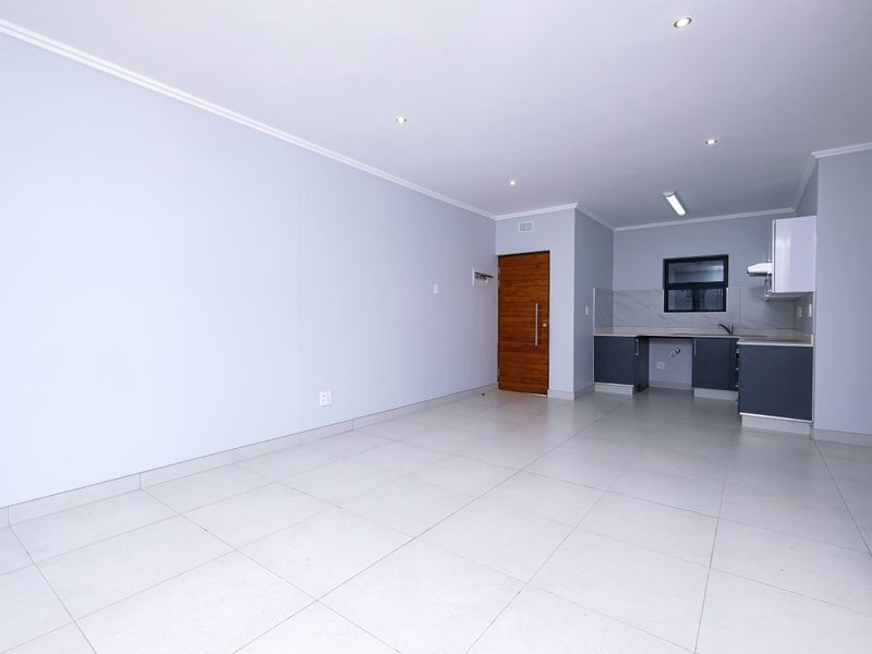 A bright, open-plan living and kitchen area featuring neutral tiled flooring, modern cabinetry, and recessed lighting, presenting a clean and well-maintained space.