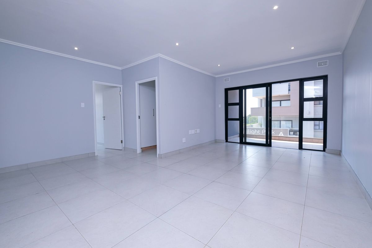 A bright, spacious, and empty living area featuring neutral tiled flooring, recessed lighting, and large sliding glass doors leading to an outdoor balcony.