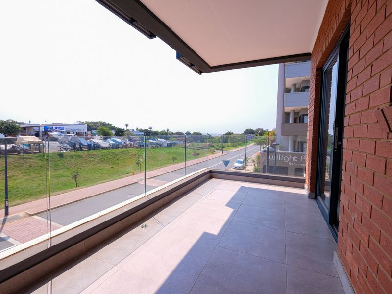 A modern, spacious balcony featuring tiled flooring, a sleek glass balustrade, and an exposed brick feature wall, offering an open outlook.