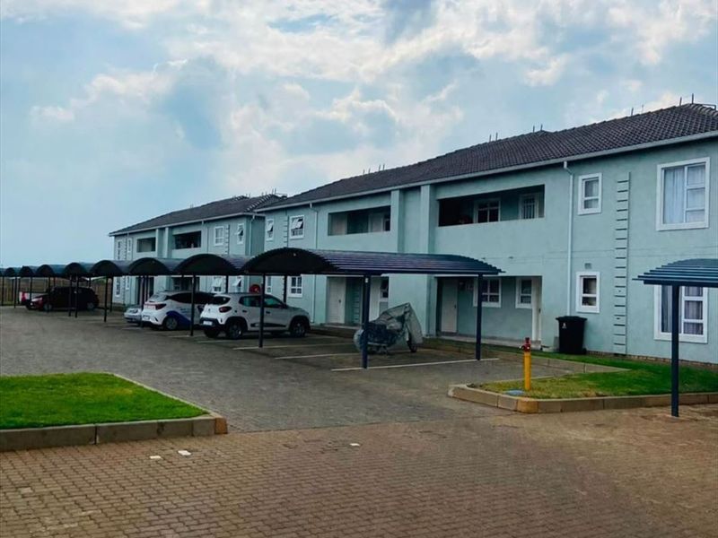 Exterior view of an apartment complex featuring covered parking bays, paved driveway, and well-maintained building facades.