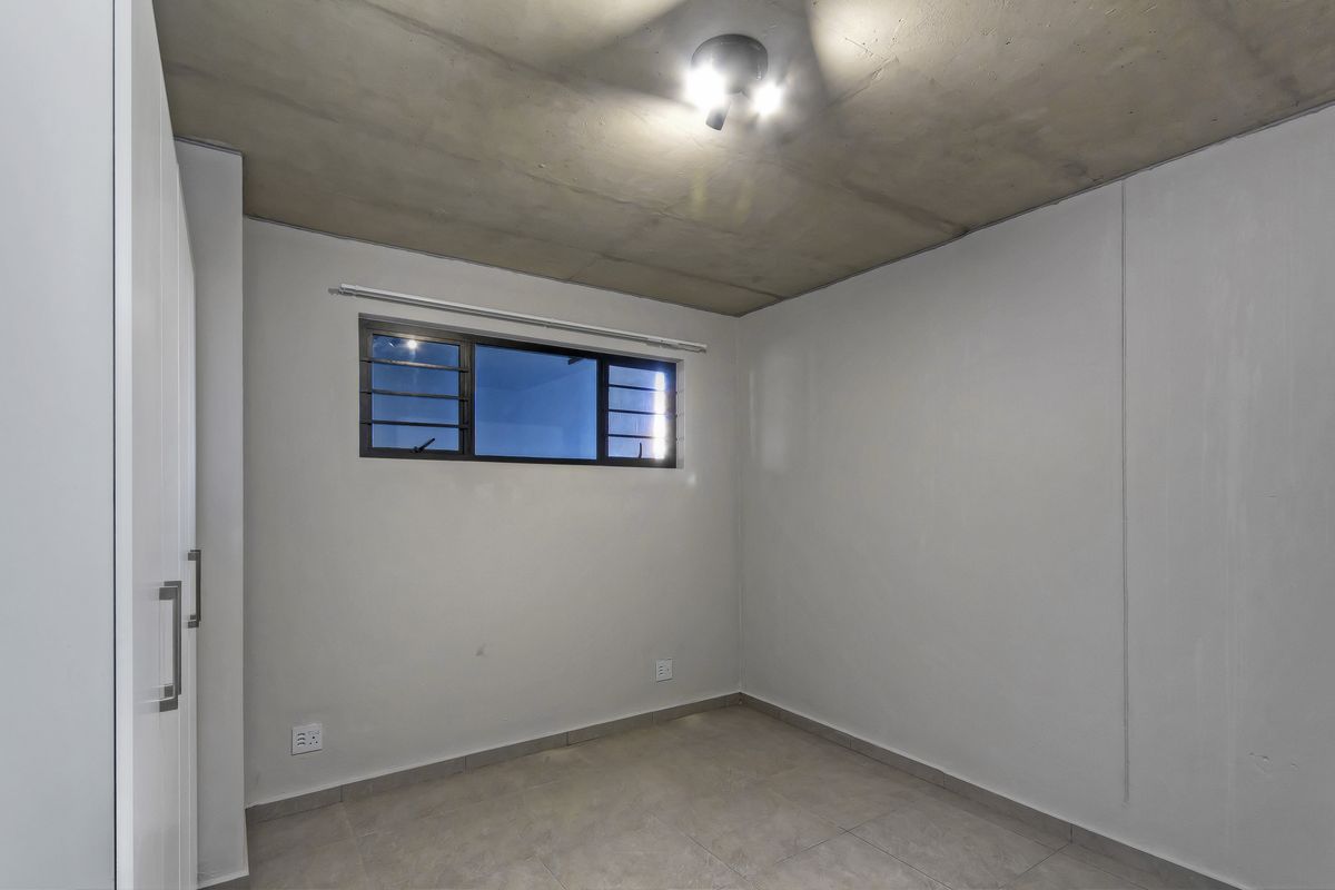 An empty bedroom featuring tiled flooring, a built-in wardrobe, and an exposed concrete ceiling, providing a neutral canvas for personalization.