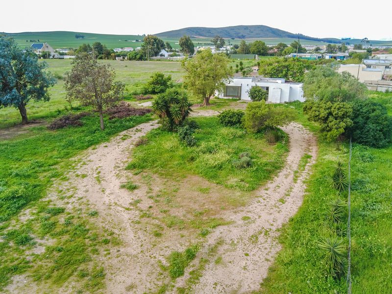 Aerial view of a large residential plot featuring an unpaved driveway, established trees, and expansive garden space surrounding the main dwelling.