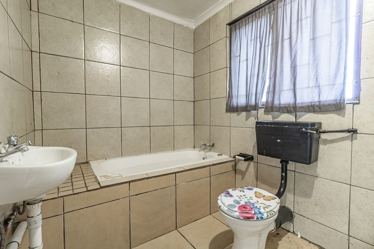 A dated bathroom featuring a bathtub, pedestal basin, and high-level cistern toilet with full-height ceramic wall tiling.