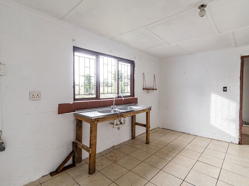 A basic, empty scullery area featuring a double stainless steel sink, tiled flooring, and security bars on the window.