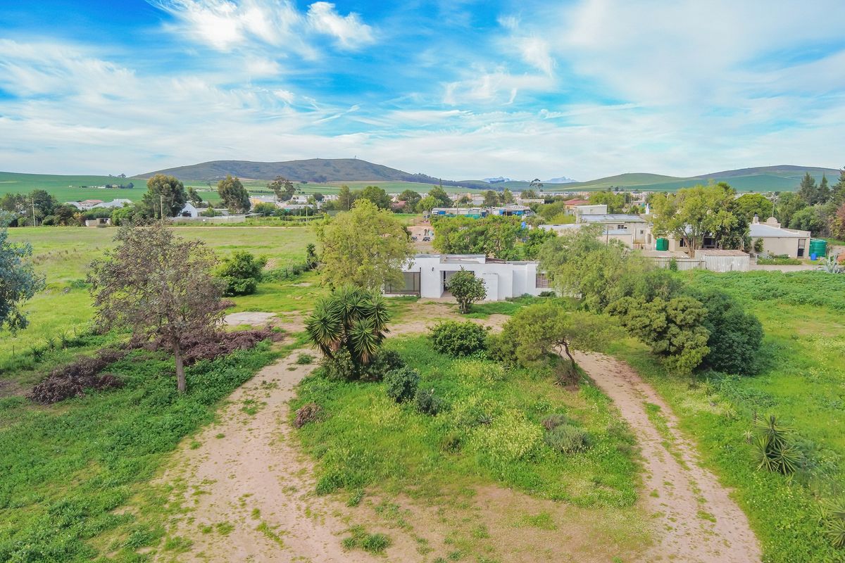 Aerial view of a residential property featuring a large plot of land with mature trees and an unpaved driveway approach.