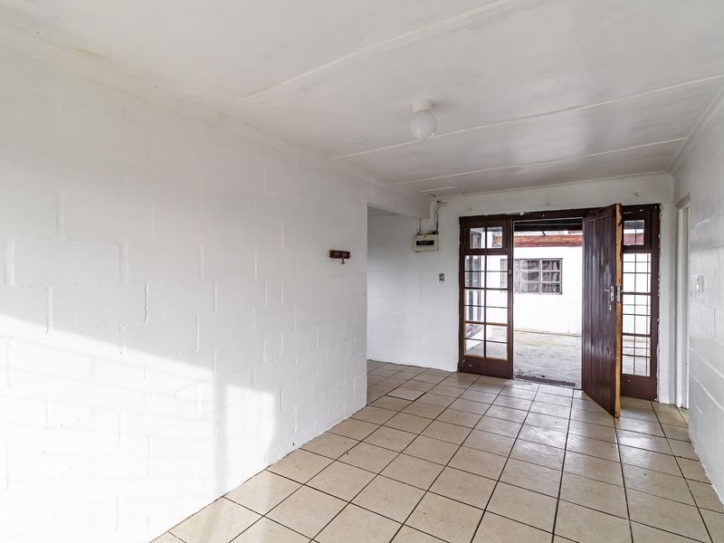 An empty entrance area featuring tiled flooring, exposed brick walls, and a timber-framed glass door leading to the exterior.