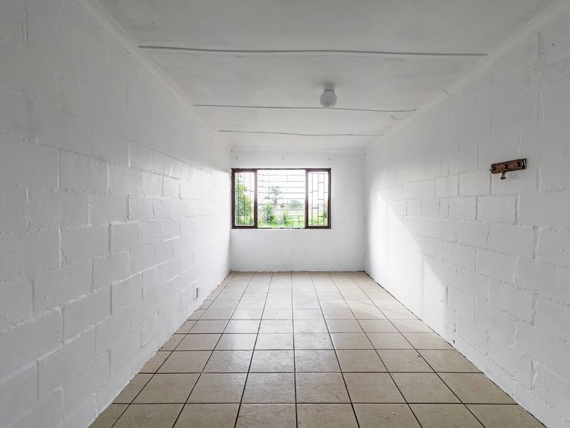 An empty bedroom featuring tiled flooring, painted blockwork walls, and security bars on the window, offering a blank canvas for renovation.