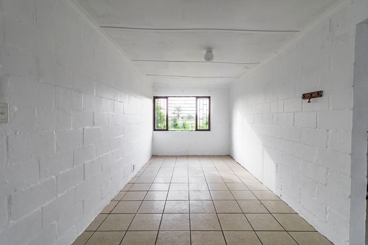 An empty bedroom featuring tiled flooring, painted blockwork walls, and security bars on the window, offering a blank canvas for renovation.