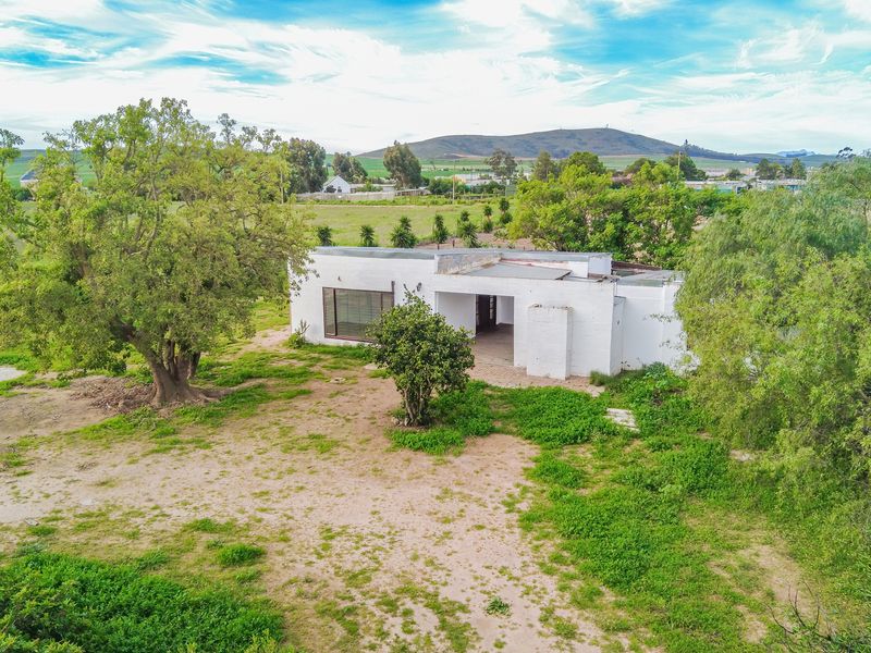 Aerial view of a single-story detached house set on a large plot with mature trees and rural surroundings.
