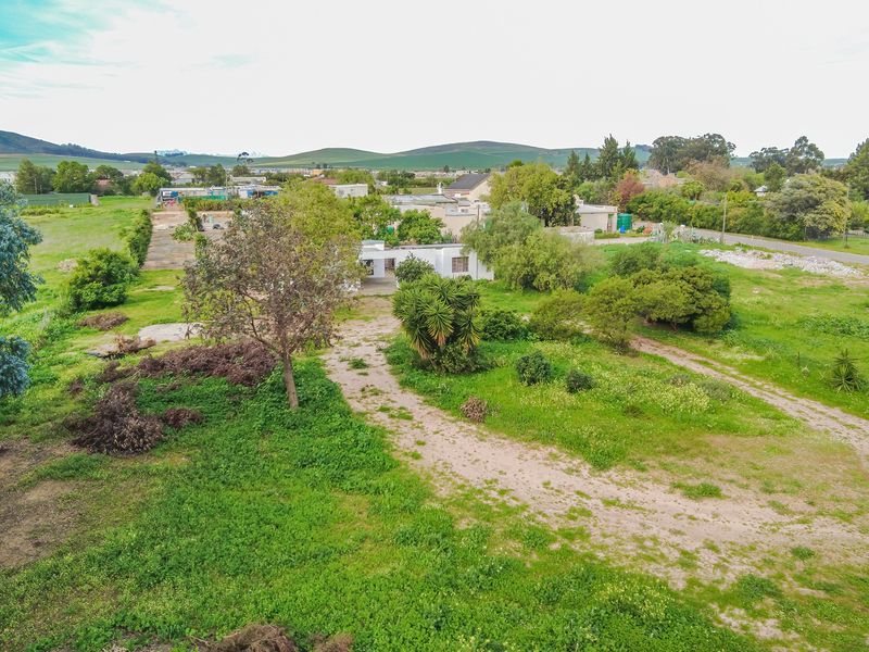 Aerial view of a large residential plot featuring an unpaved driveway, extensive garden space, and mature trees in a rural setting.