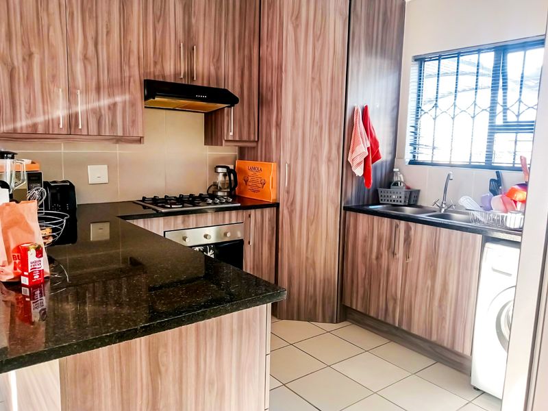 Modern kitchen featuring wood-grain cabinetry, granite countertops, gas hob, built-in oven, and a double sink with security bars on the window.