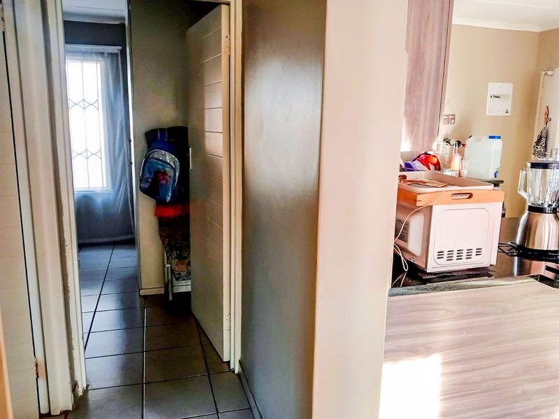 A view from the kitchen area looking into a tiled hallway leading towards a bedroom with a window.