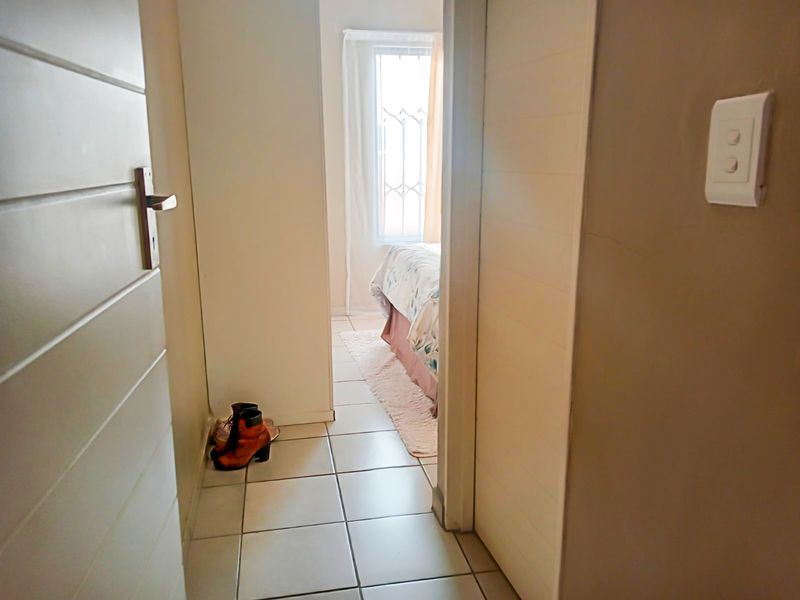 A functional hallway with tiled flooring leading into a bedroom, featuring standard internal doors and a wall-mounted light switch.