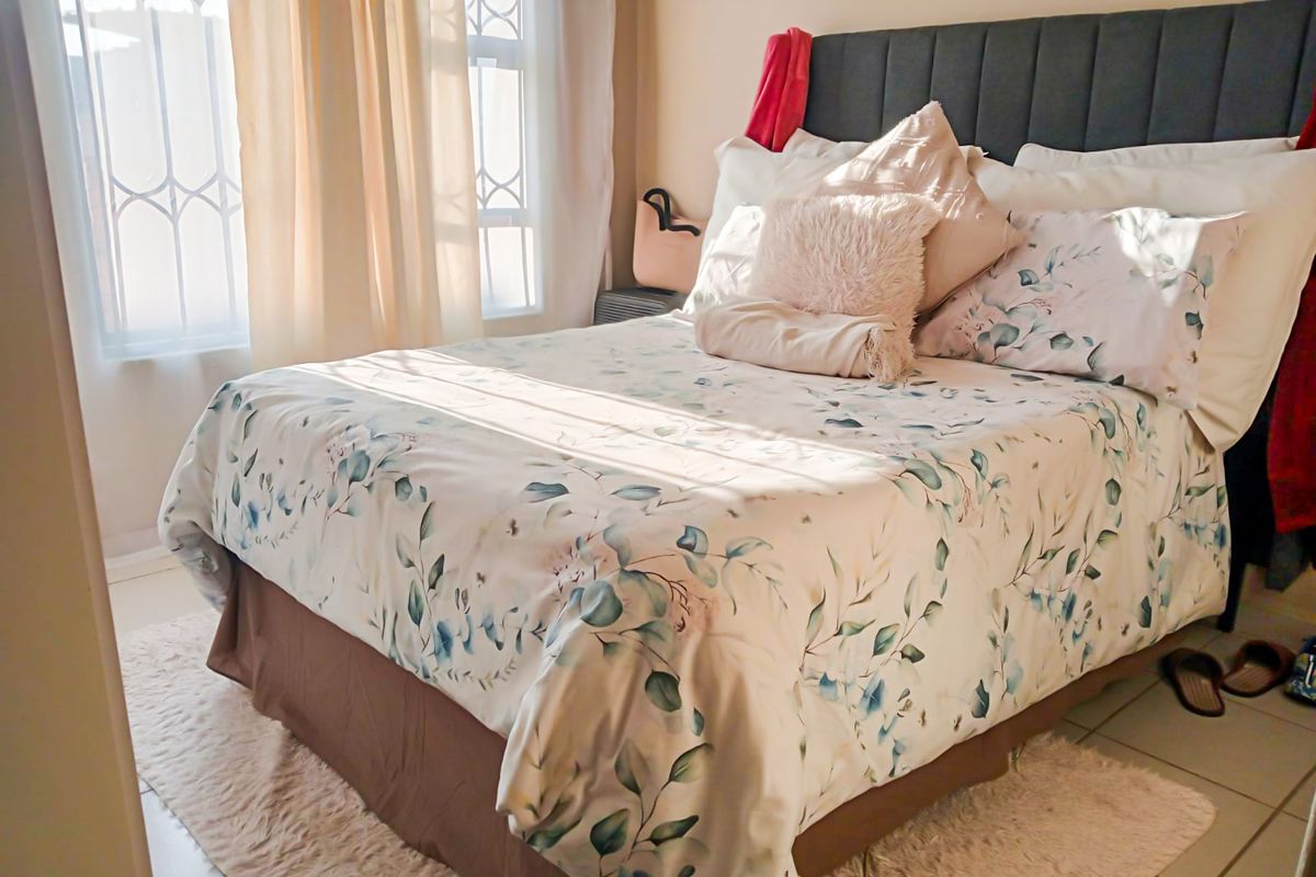 A cozy bedroom featuring tiled flooring and windows fitted with security bars, allowing for natural light.