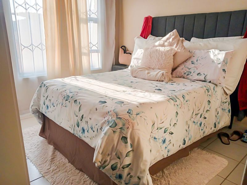 A cozy bedroom featuring tiled flooring and windows fitted with security bars, allowing for natural light.
