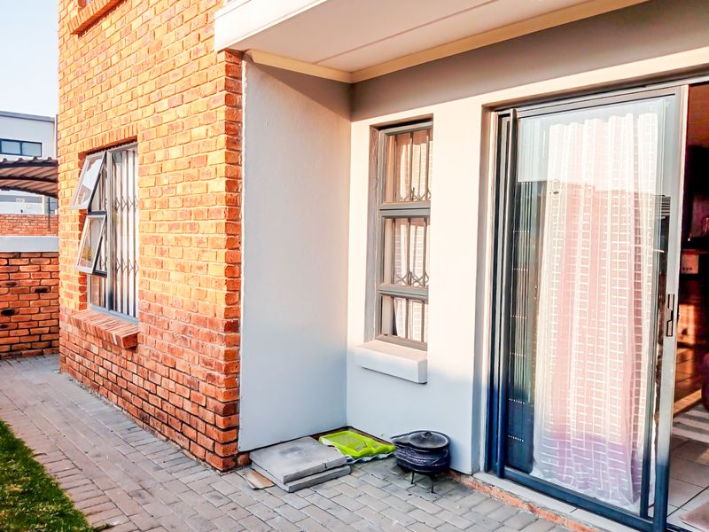 A view of the rear exterior featuring exposed brickwork, a paved patio area, and a sliding glass door providing access to the interior.