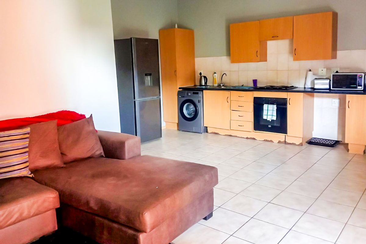 Open-plan living area featuring a functional kitchen with built-in cabinetry, integrated oven, hob, and tiled flooring throughout.