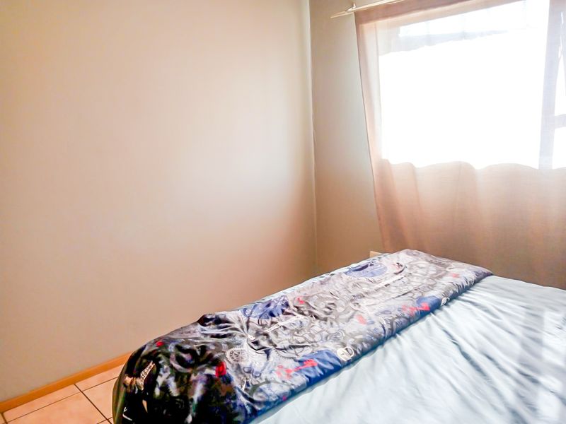 A simple bedroom featuring tiled flooring and a window allowing natural light into the space.
