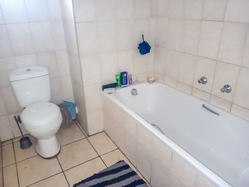 A functional bathroom featuring a standard bathtub and toilet with neutral wall and floor tiling.