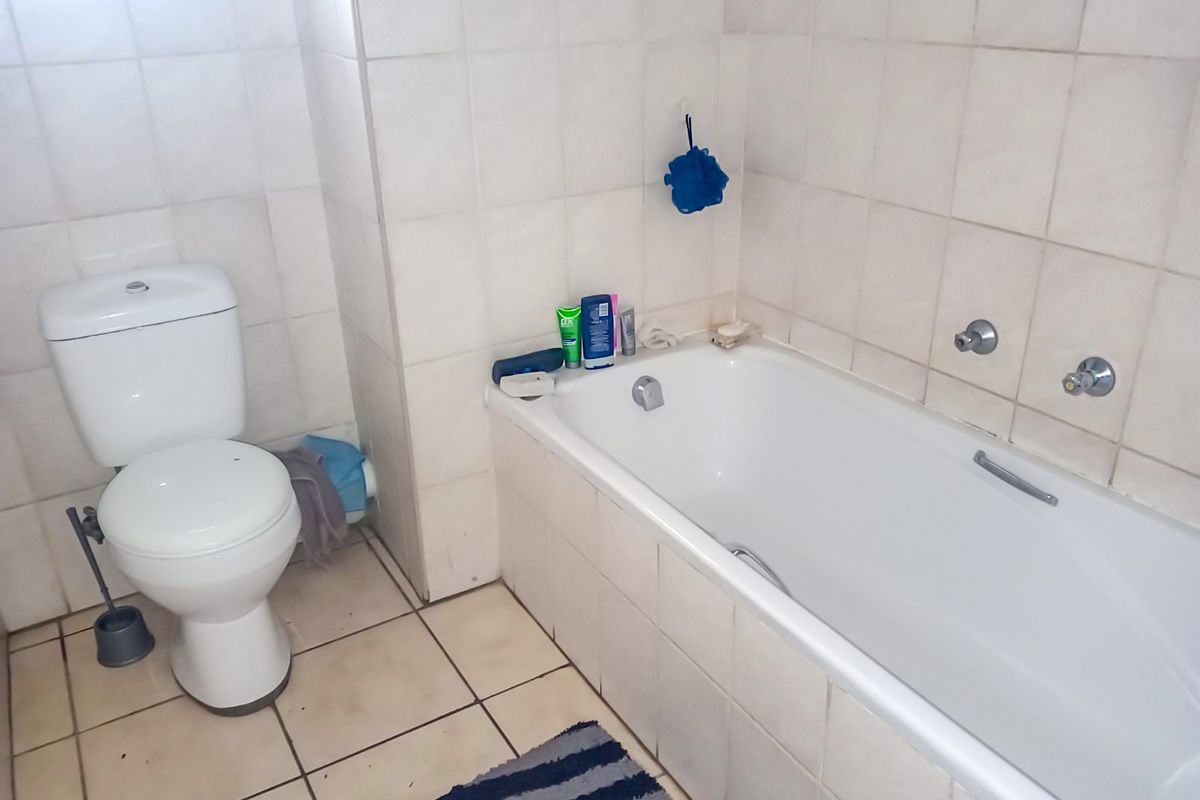 A functional bathroom featuring a standard bathtub and toilet with neutral wall and floor tiling.