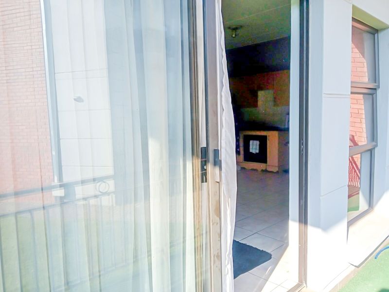 A view from a balcony looking through a sliding glass door into an interior living space with tiled flooring.