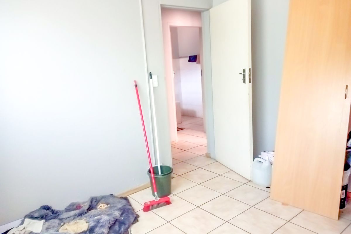 A simple bedroom featuring tiled flooring and a built-in cupboard, with a doorway leading to an adjacent room.