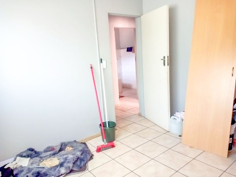 A simple bedroom featuring tiled flooring and a built-in cupboard, with a doorway leading to an adjacent room.