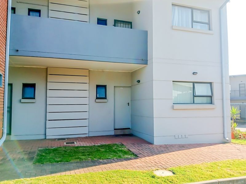 Front elevation of a modern apartment building featuring a paved entrance area, balcony, and contemporary exterior finishes.