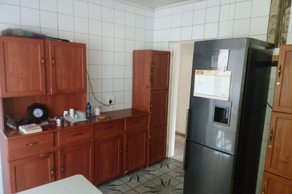 A dated kitchen area featuring wooden cabinetry, tiled wall splashbacks, and tiled flooring, requiring cosmetic updates to modernize the space.