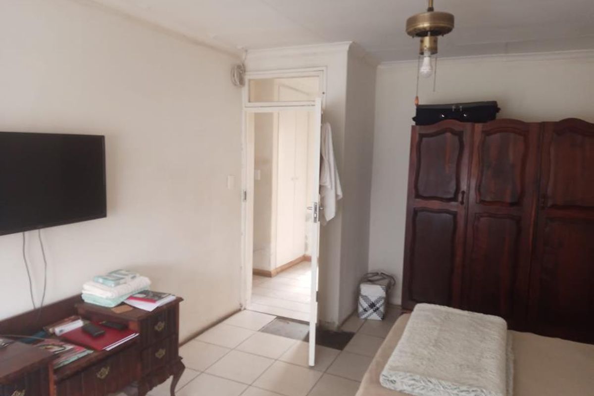 A bedroom featuring tiled flooring and a doorway leading to an adjacent hallway, showing signs of wear on the walls and ceiling.