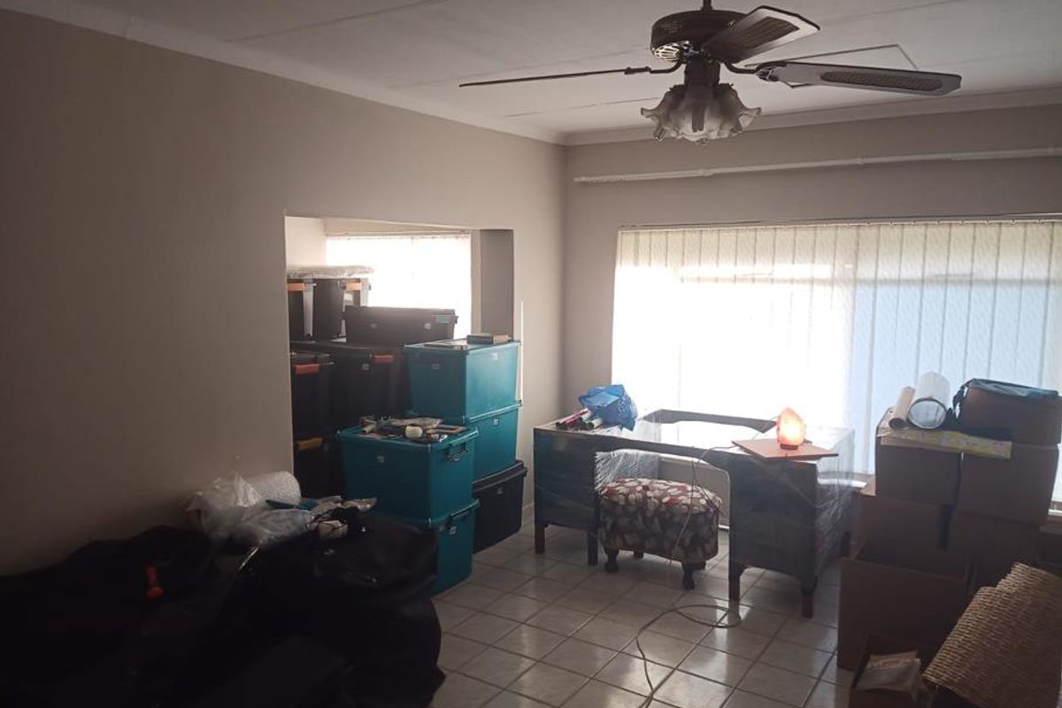 A living area featuring tiled flooring, a ceiling fan, and vertical blinds, currently used for storage.